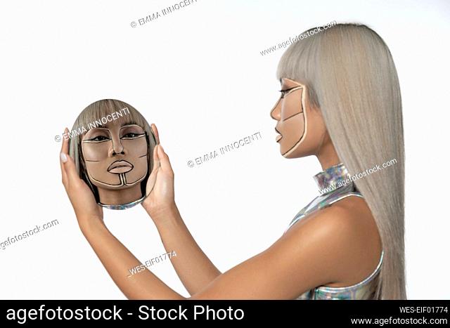 Cyborg woman looking at reflection in mirror against white background