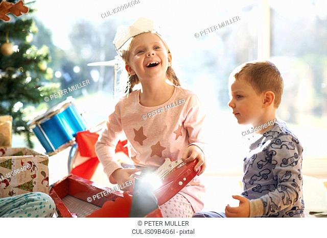 Excited girl and brother on living room floor with toy guitar christmas gift