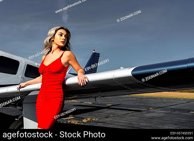 A gorgeous young blonde model poses outdoors with a single engine aircraft at a local airport