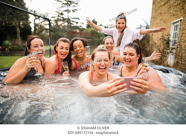 Small group of female friends enjoying a weekend away. They are taking a group selfie while sitting in a hot tub