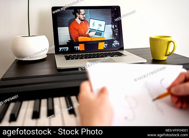 Mid adult woman writing musical notes during online tutorial on laptop at home