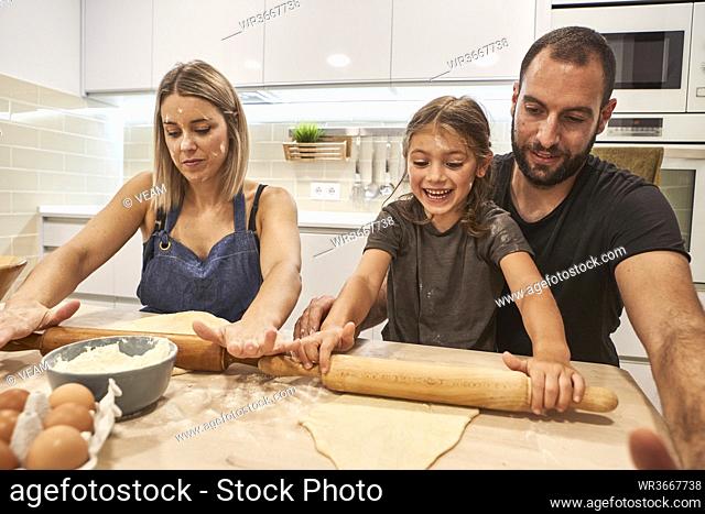 Happy family kneading pizza dough with rolling pins on table in kitchen