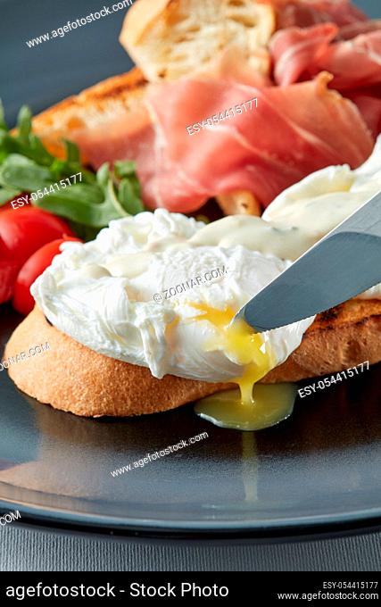 Fresh toast sandwiches with Poached egg, tomato, salad and bacon on plate, knife cutting an egg