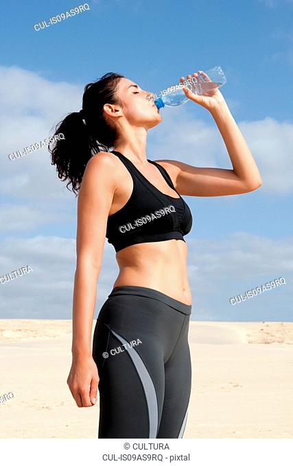 Mid adult woman drinking from water bottle whilst exercising at beach