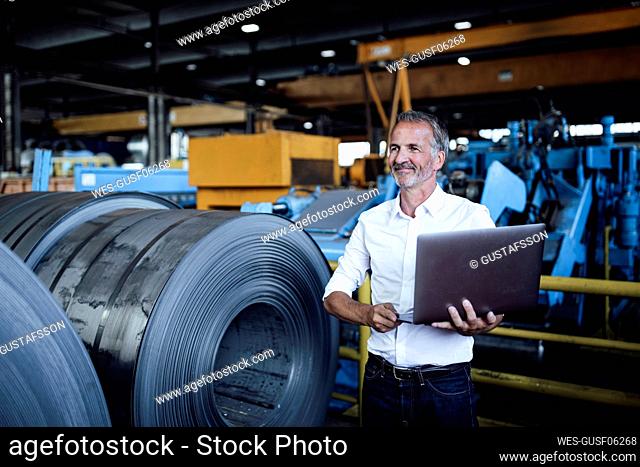 Smiling businessman holding digital tablet in steel mill