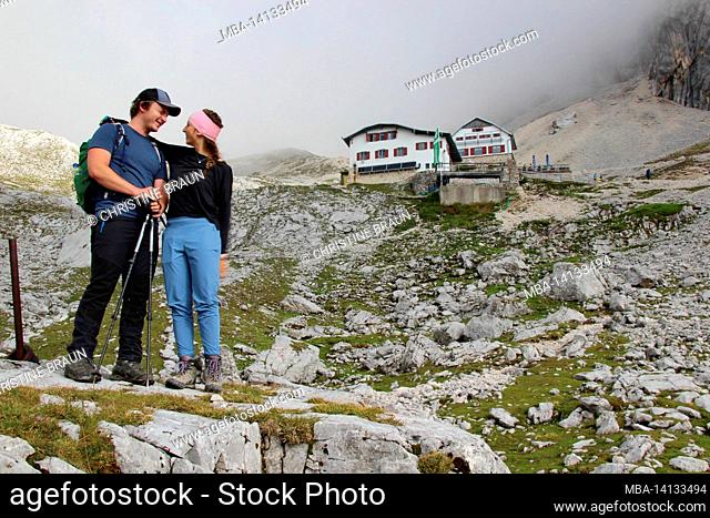young couple on hike to zugspitze 2962 m, in the background the knorrhütte (2051m) in the early morning fog, wetterstein mountains garmisch-partenkirchen