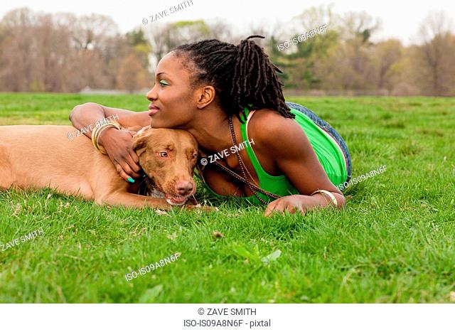 Young woman and her dog lying on grass