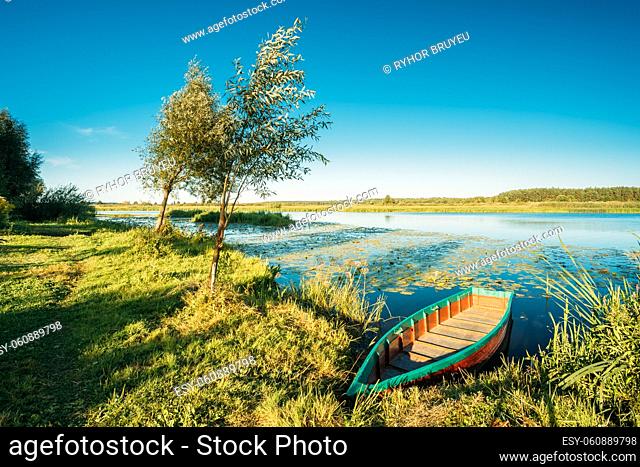 Lake Or River And Old Wooden Blue Rowing Fishing Boat At Beautiful Summer Sunny Day Or Evening. Sunny Clear Blue Sky. Typical Nature Of Belarus And Western...
