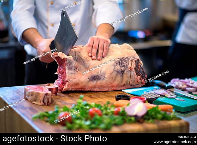 chef using ax while cutting big piece of beef on wooden board in restaurant kitchen