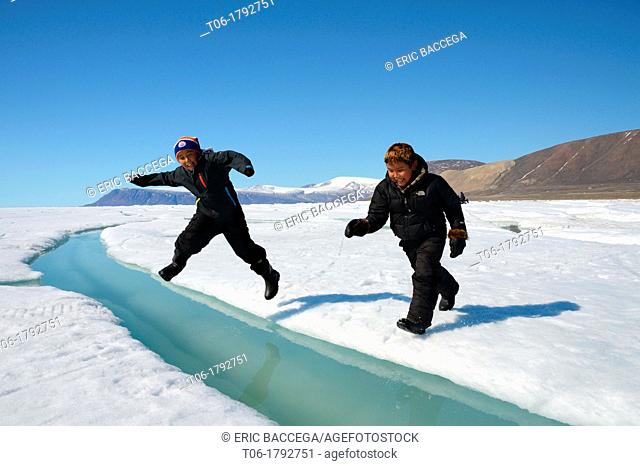 Two young Inuit boys jumping over a crack on ice floe Ellesmere island, Nanavut, Canada