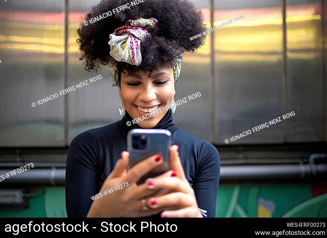 Happy fashionable young woman using mobile phone against wall