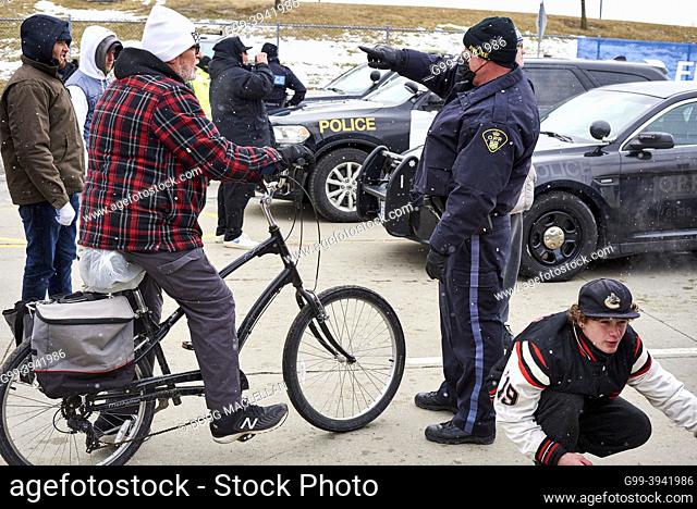 A man on a bike is directed by a police officer to another route to attend the Freedom Convoy blockade of the Ambassador Bridge on 12 February 2022 in Windsor