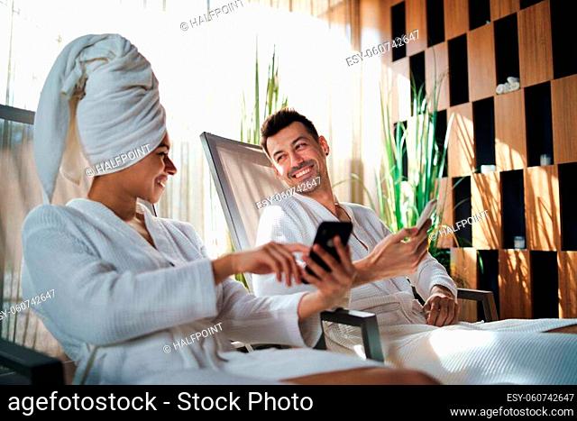 A portrait of young couple relaxing in spa resort, using smartphone