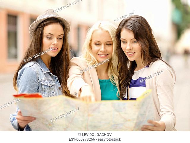 holidays and tourism concept - three beautiful girls looking into tourist map in the city