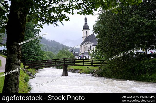 09 June 2022, Bavaria, Ramsau bei Berchtesgaden: Rain clouds hang over the church of St. Sebastian at the painter's corner