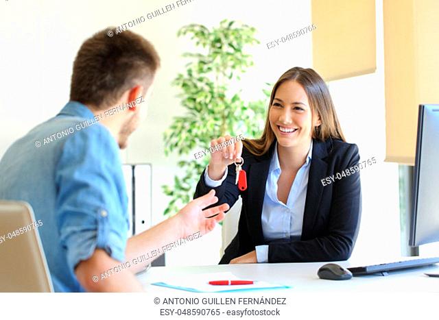Happy real estate agent giving house keys to a customer after signing contract in the office