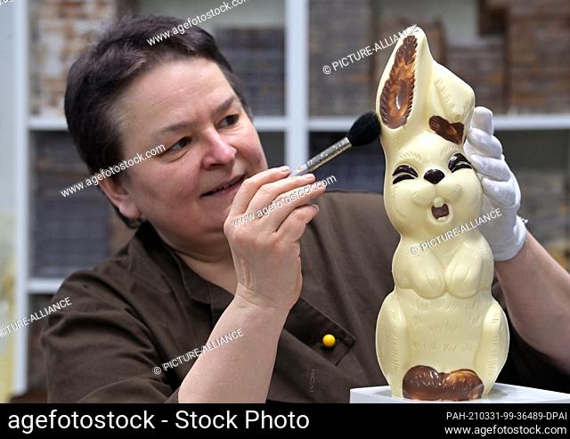 30 March 2021, Brandenburg, Himmelpfort: Sylke Wienold, head of the Himmelpforter Chocolaterie, removes disturbing particles from a bunny made of light...