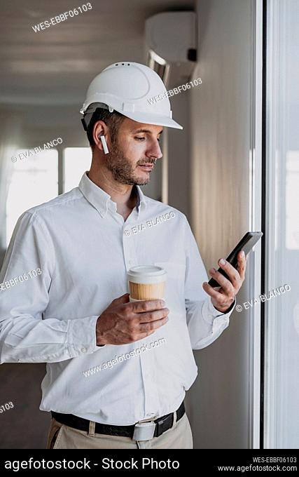 Engineer holding disposable cup looking at mobile phone in office