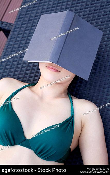 Young woman in a swimsuit lying down and relaxing with a book over her face