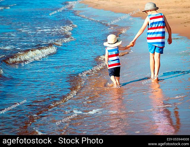 Two brothers barefoot are walking on the beach in water. Boys are on vacation in summer at the sea