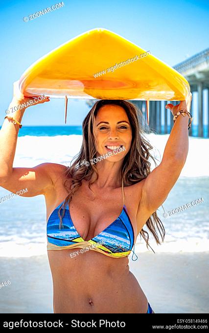 A beautiful brunette bikini model her surfboard on a beach