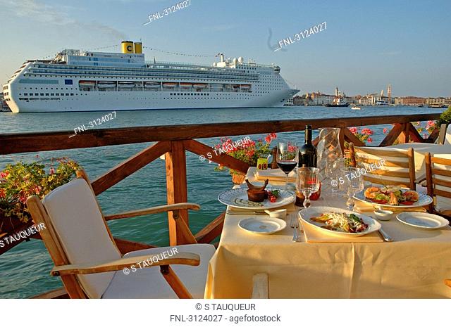 Chairs and tables on the Hotel Cipriani terrace, cruise ship passing by, Giudecca, Venice, Italy