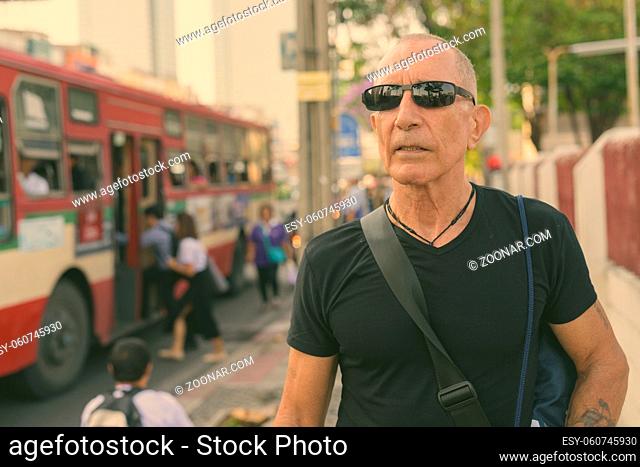 Portrait of bald senior tourist man at the bus stop in the city