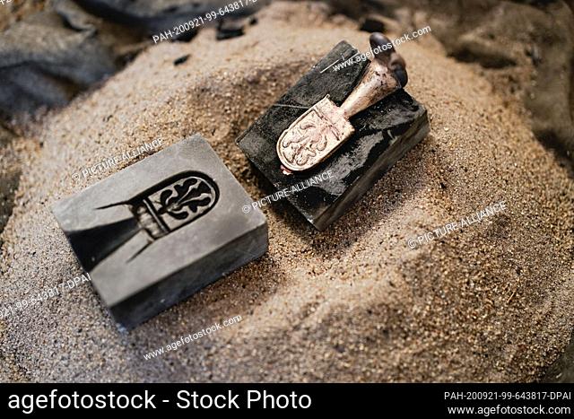15 September 2020, Hessen, Lorsch: A cast piece of bronze is stuck in a soapstone mould lying on a pile of sand in the Lauresham open-air laboratory at a...