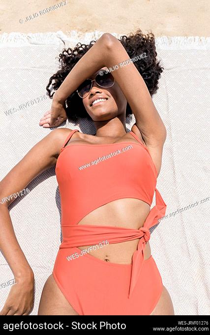 Smiling young woman covering face with hand while lying at beach on sunny day