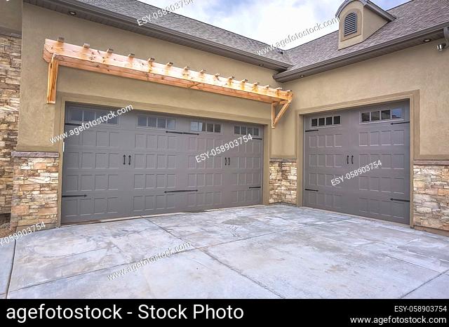 Exterior of a home with view of gray double garage doors and stone wall. A wood awning is built over one of the glass paned garage doors