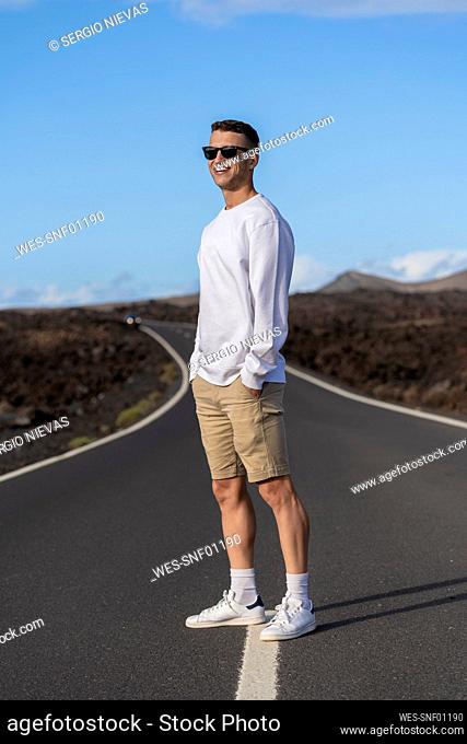 Smiling male tourist with hands in pockets standing on road
