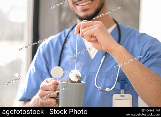 Cropped photo of a smiling pleased physician placing a teabag in a ceramic cup with boiling water