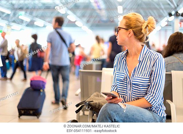 Casual blond young woman using her cell phone while waiting to board a plane at departure gates at international airport