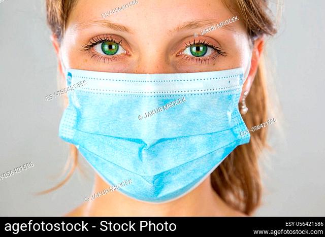 Close-up of alert young blonde woman with face mask looking into camera. Attentive girl with protection over mouth and nose from front view in vertical...