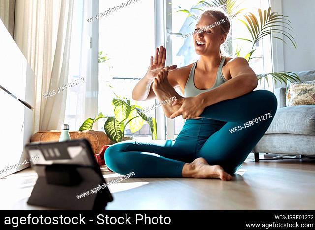 Smiling woman doing yoga while learning through digital tablet at home