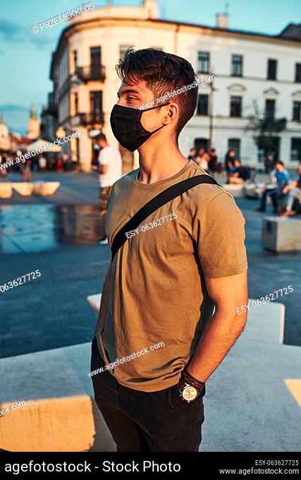 Young man standing in the city center, looking away, wearing the face mask to avoid virus infection and to prevent the spread of disease in time of coronavirus