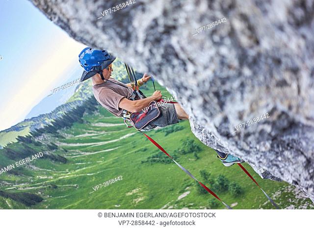 man climbing and preparing backup anchor point for stretching the highline slackline rope in Bavarian alps, near mountain Blankenstein, south of Germany