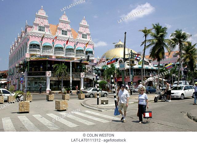 Dutch Antilles. Town. Large gabled building. Pink paintwork. Dome. Palm trees. Pedestrian crossing. Two people. Person on bicycle