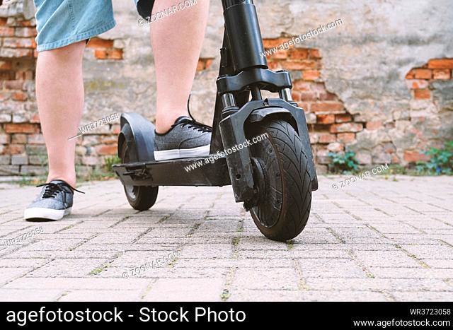 legs of unrecognizable man wearing shorts with electric kick scooter or e-scooter - e-mobility or micro-mobility hipster lifestyle trend