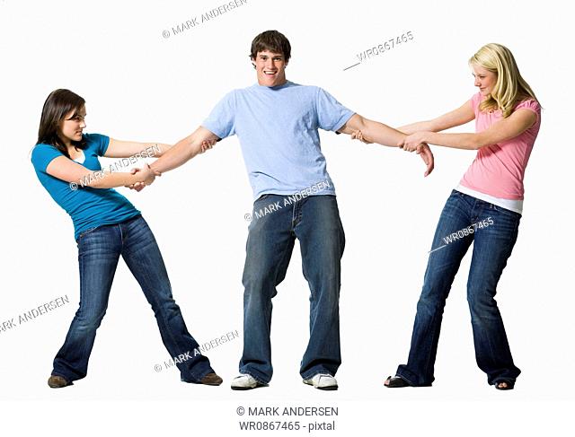 Two girls tugging at arms of boy