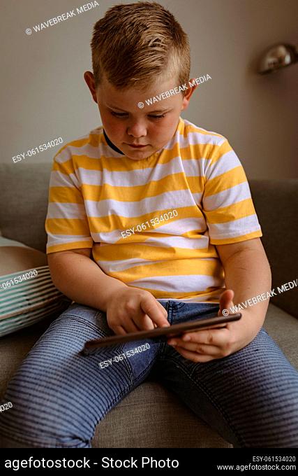 Caucasian boy using digital tablet sitting on the couch at home