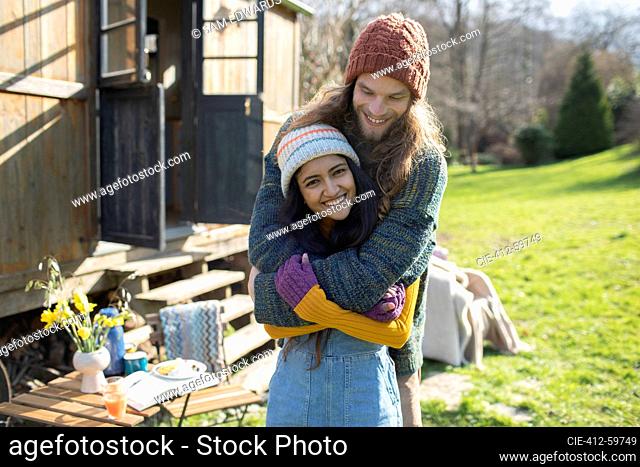 Portrait carefree young couple hugging outside sunny cabin rental