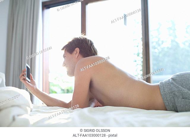 Man lying in bed using multimedia smartphone