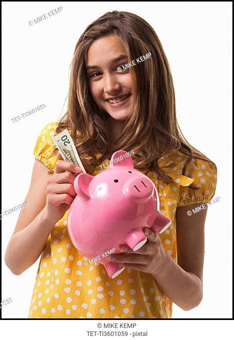 Teenage girl putting money in piggy bank