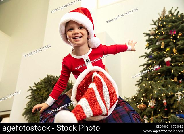 Young boy held up above his fathers head, playing by Christmas tree