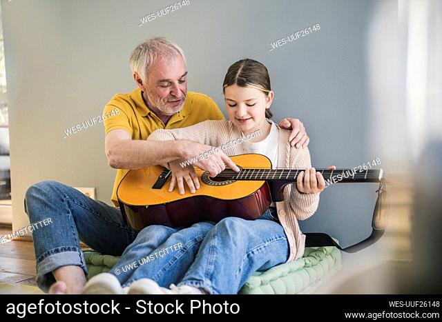 Happy senior man teaching guitar to granddaughter at home