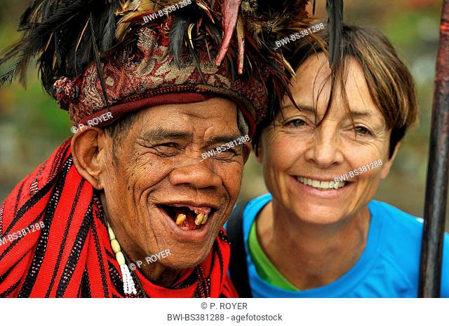 portrait of an old man with a few teeth in traditional clothing of Ifuago tribe and a female tourist smile for the camera, Philippines, Luzon, Banaue