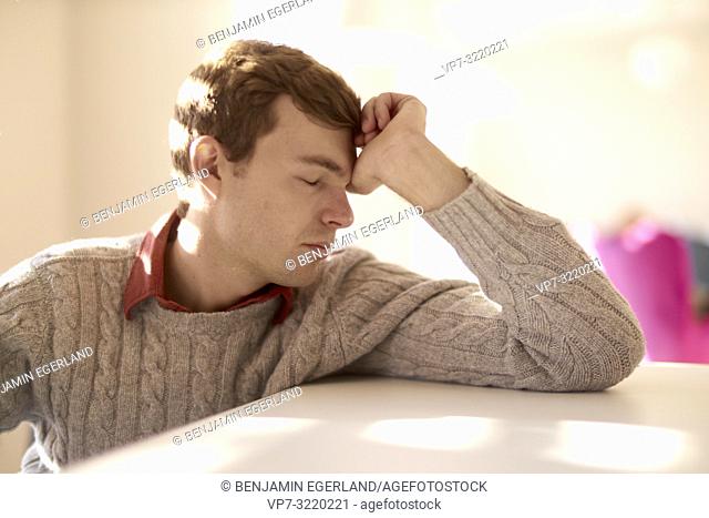 Young man at table with closed eyes, indoors, student, business man, office