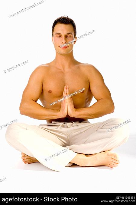 Young attractive man sitting yoga style. He's eyes closed. White background in studio