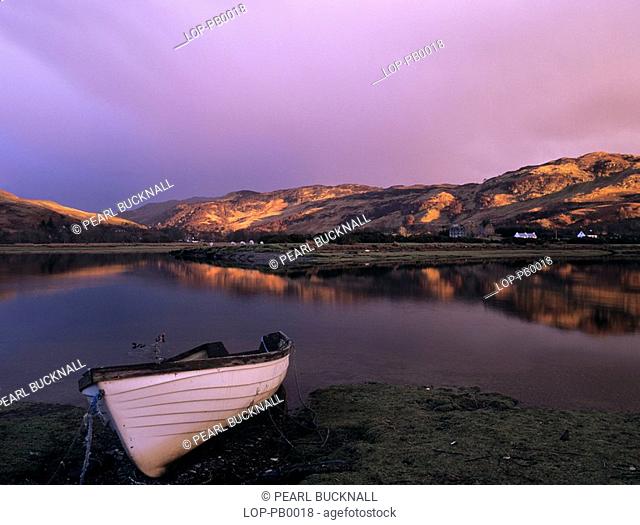 Scotland, Highland, Glenelg, Dusk over the Glenmore river estuary at high tide, with a boat on the foreshore and the last rays of sun on the hills beyond